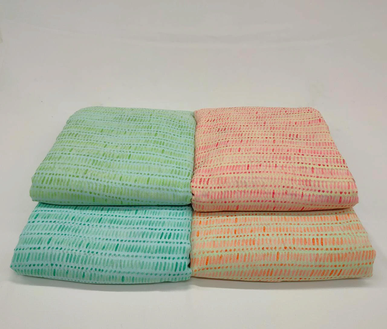 Folded handloom base cloths in mint, peach, blue, and cream