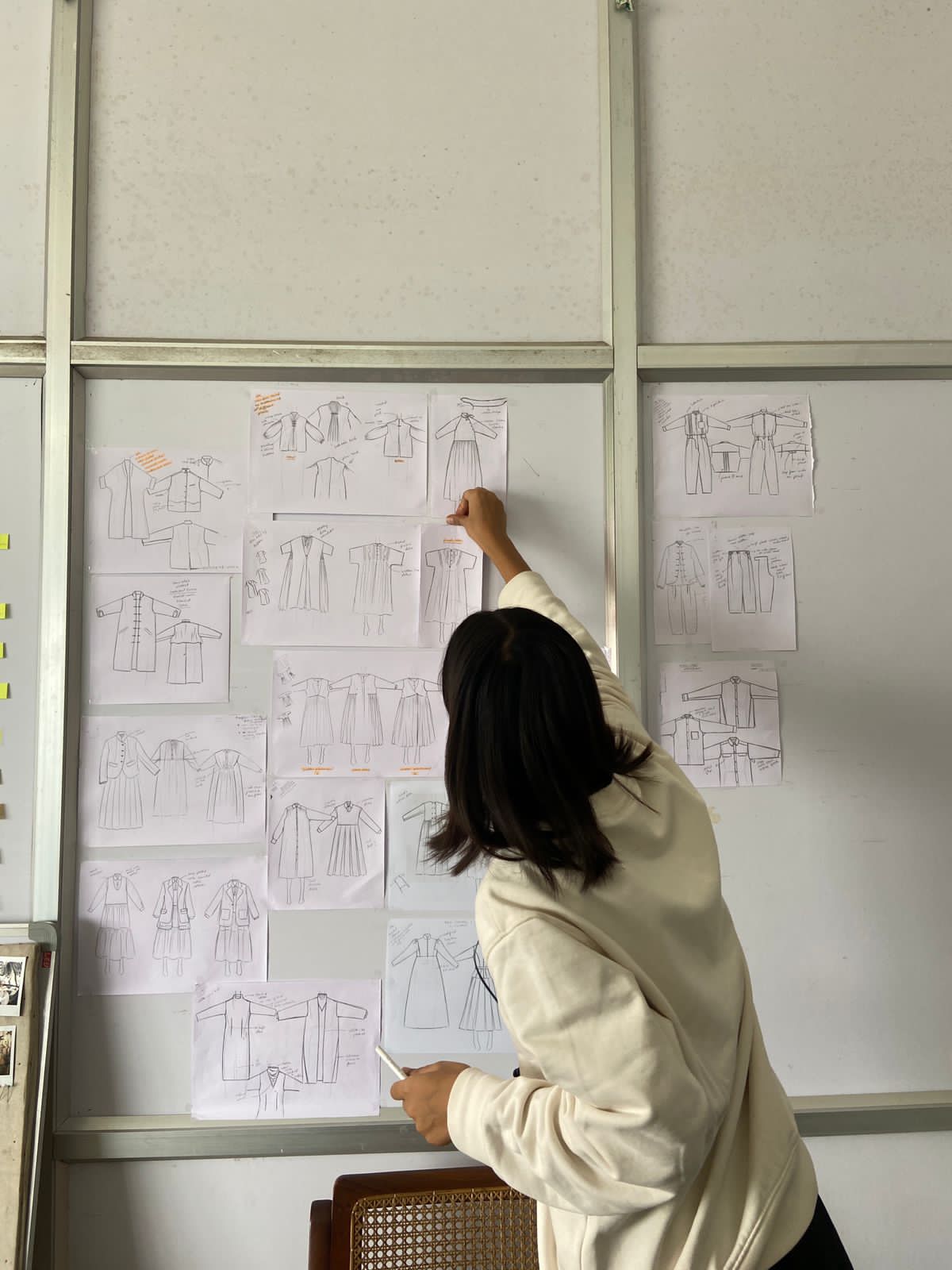 Mansi Pandey pinning fashion sketches across a studio design wall